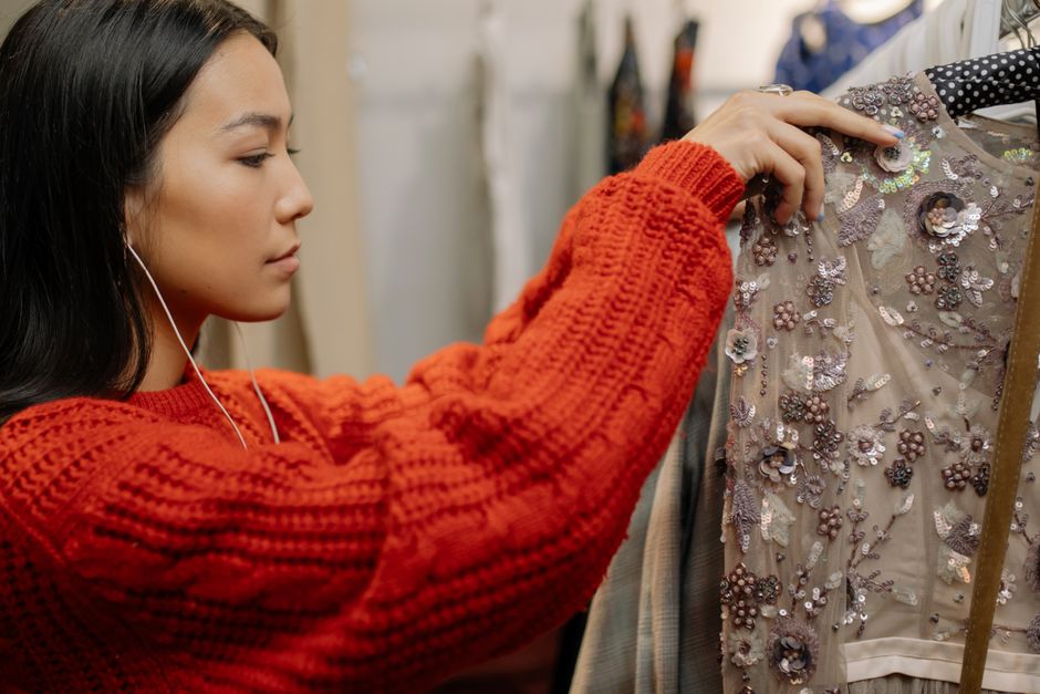 Asian woman in a fashion store choosing clothes, wearing red knitwear, indoors.